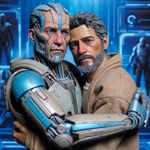 A Caucasian male figure with distinct facial features wearing lightly colored futuristic clothing with blue accents is embracing a man of Middle-Eastern descent who has scruffy facial hair and casual clothing. The backdrop is a bluish, sleek and technologically advanced setting in a dystopian type future.